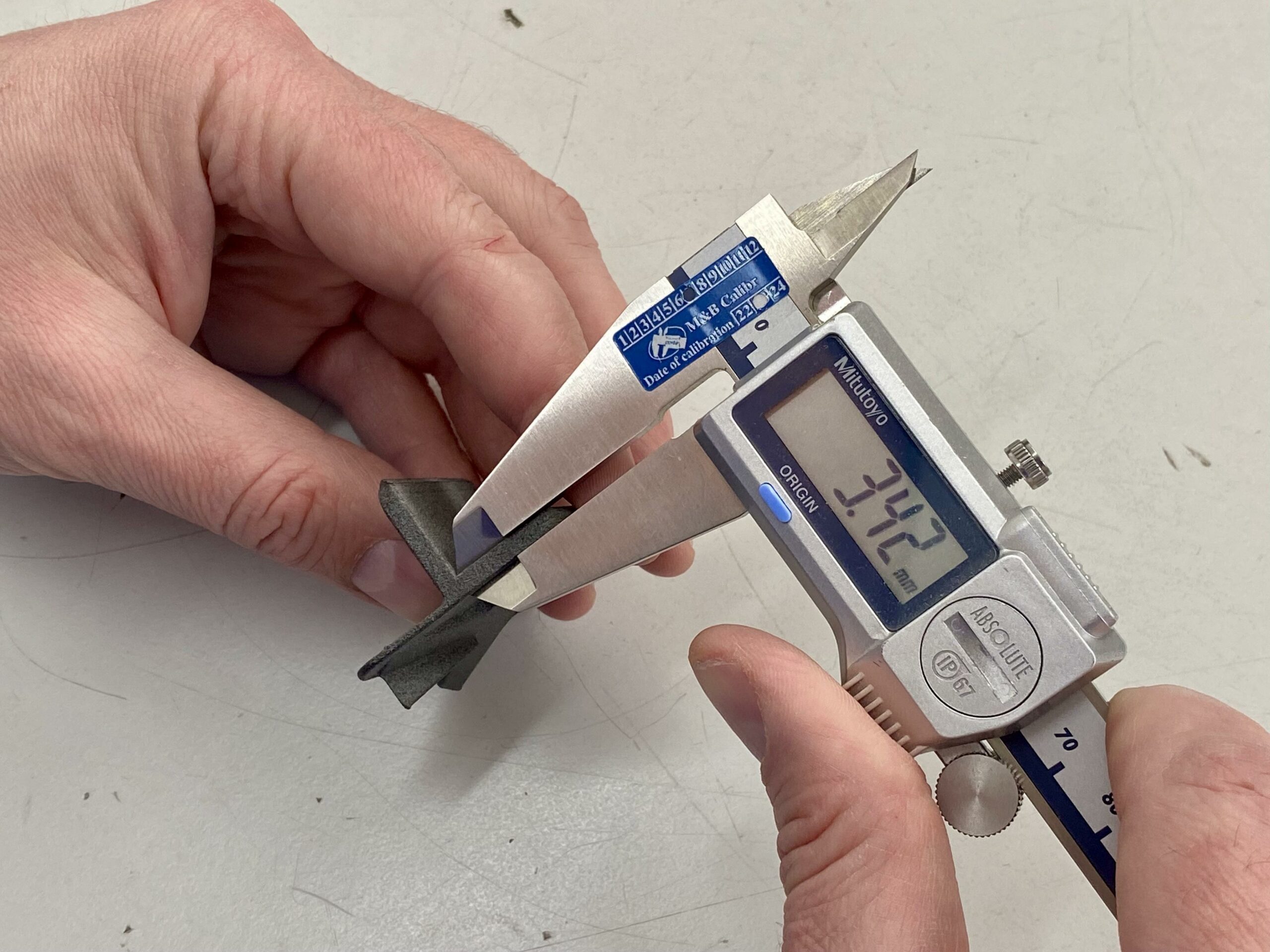 A person using a digital caliper to measure the thickness of a black 3D-printed part, with the caliper