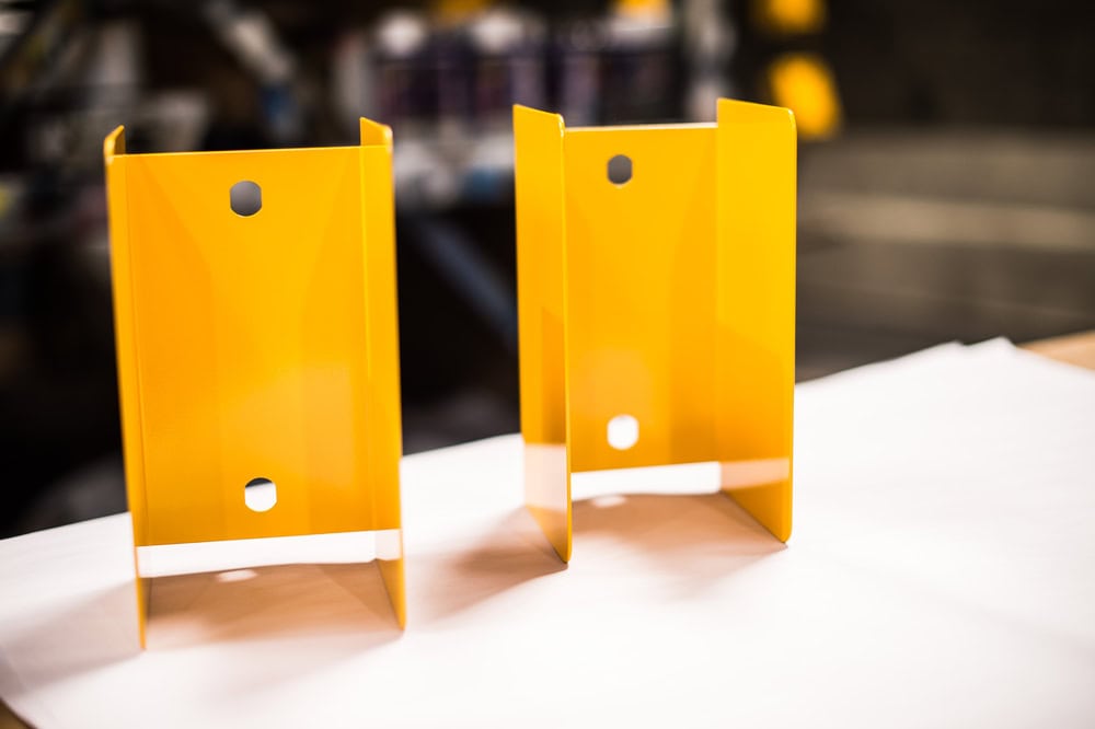 Two yellow powder-coated metal brackets with a glossy finish