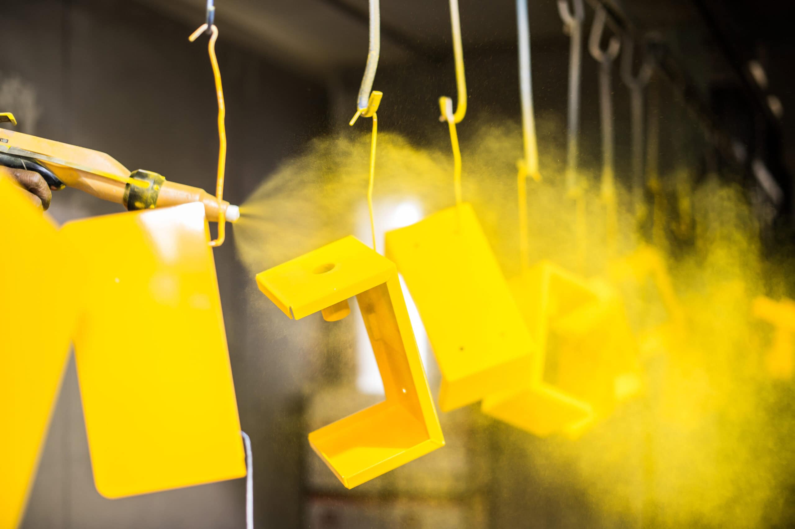Yellow powder coating being applied to metal parts suspended on hooks