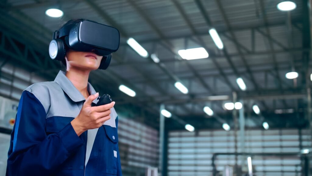 Technicien industriel portant un casque de réalité virtuelle et tenant une manette dans une usine pour démontrer une formation de maintenance à distance.1`q