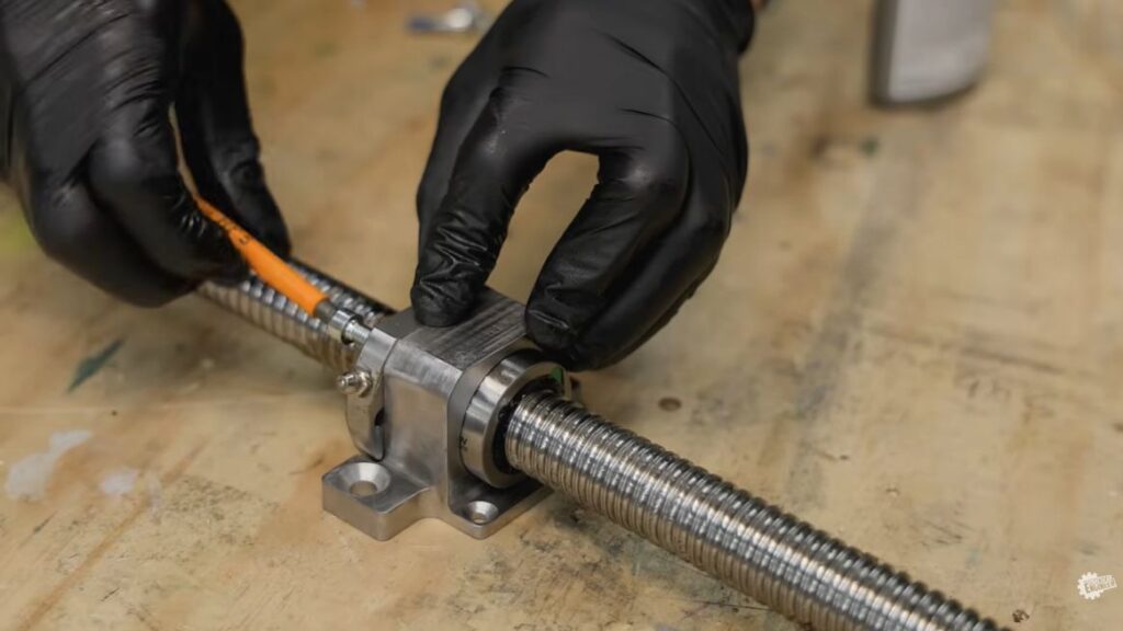 Close-up of hands assembling a ballscrew spindle nut during the Z-axis build of a custom 5-axis CNC machine