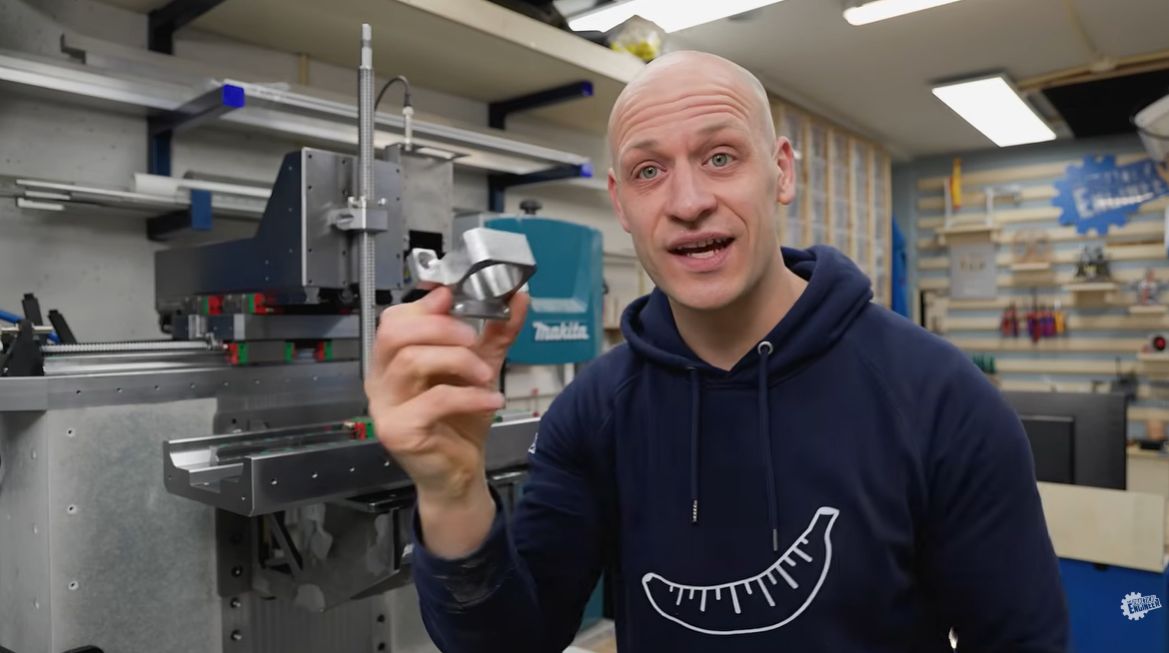Emiel Noorlander from The Practical Engineer holding the redesigned steel spindle nut mount in front of his 5-axis CNC machine